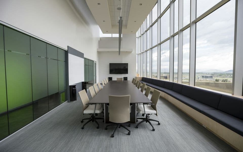 A modern conference room with a wooden table, chairs, and presentation display screen