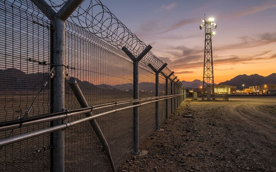 Valla de seguridad con concertina y torre de vigilancia al atardecer