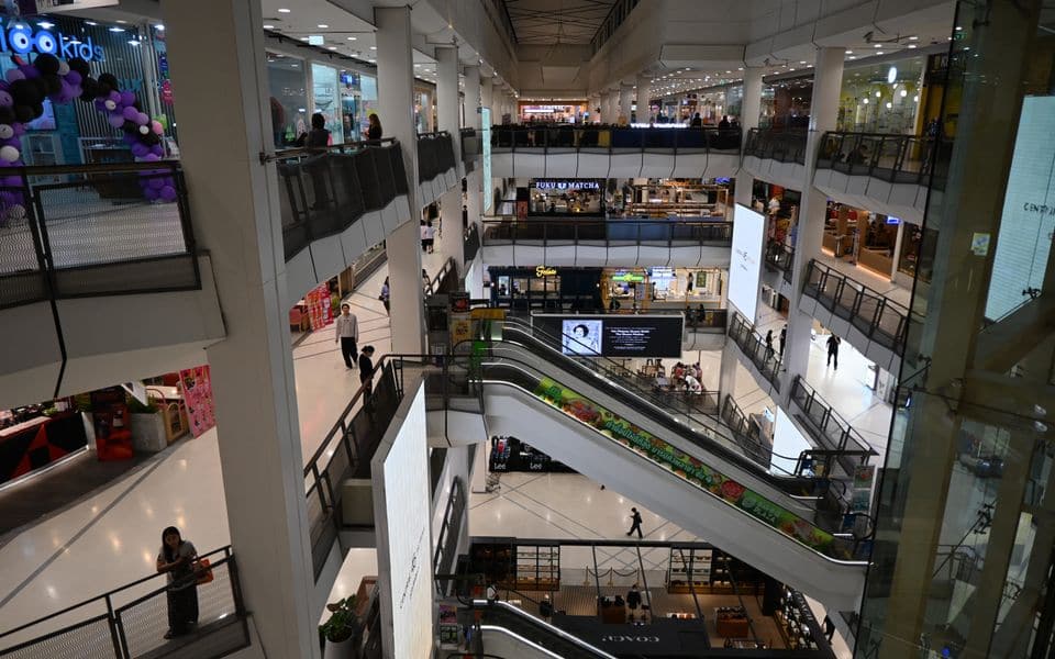 A shopping mall interior with escalators and shop fronts